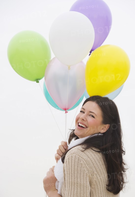 Young woman holding bunch of balloons laughing.
