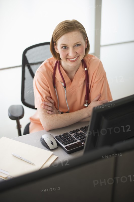 Female nurse sitting at desk and smiling.