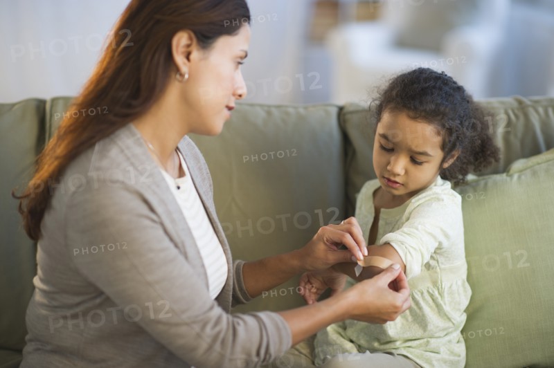 Mother applying band aid on daughter's (6-7) arm.