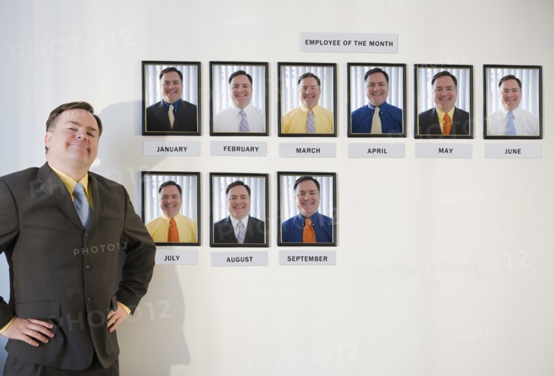 Businessman standing in front of employee of the month portraits. Photo: Jamie Grill Photography