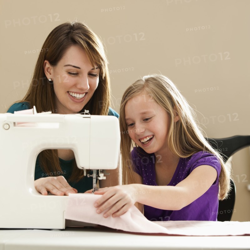 Girl (8-9) and young woman using sewing machine. Photo : Mike Kemp