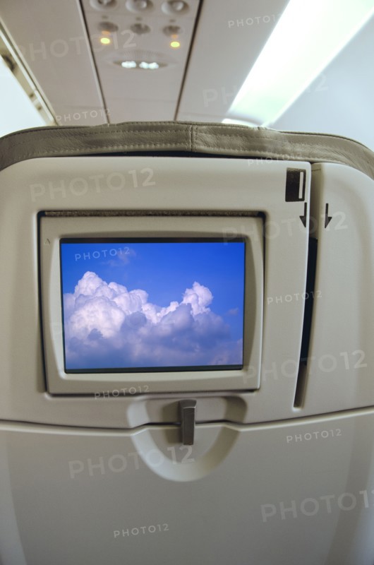 Airplane seat with monitor displaying clouds. Photo : Tetra Images