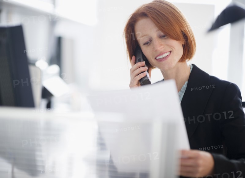 Businesswoman reading documents and talking on telephone. Photo: Jamie Grill Photography