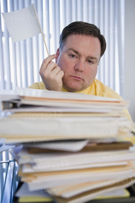 Businessman holding white flag over stack of paperwork. Photo: Jamie Grill Photography