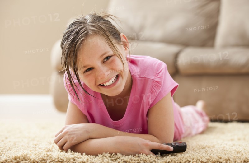 Portrait of girl (10-11) lying on floor holding remote control. Photo : Mike Kemp