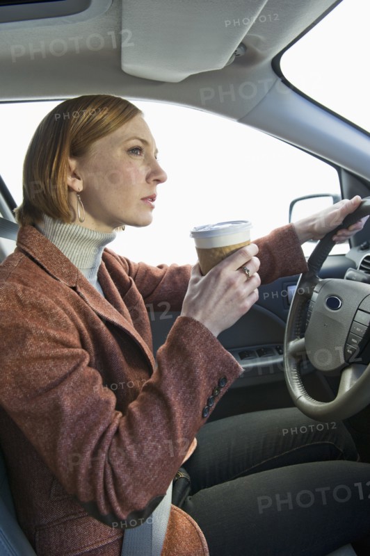 Woman driving car and drinking coffee.