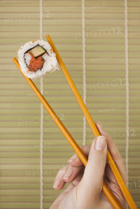 Woman holding sushi by chopsticks.