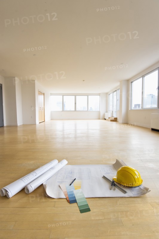 Blueprint, color swatch and hardhat on floor in empty room.