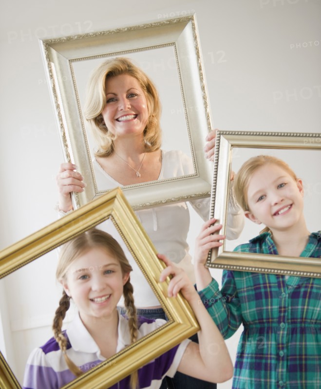 Mother and daughters (8-11) holding picture frames. Photo: Jamie Grill Photography