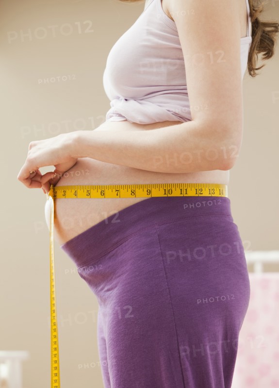 Young pregnant woman measuring belly. Photo : Mike Kemp