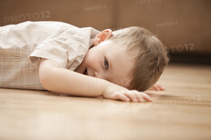 Portrait of smiling boy (2-3) lying on floor. Photo: Mike Kemp