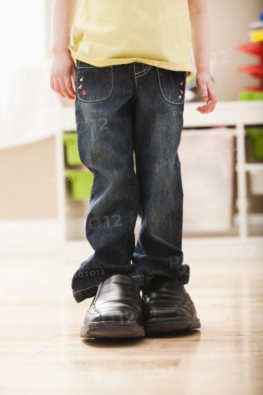 Girl (2-3) standing in dad's shoes, low section. Photo: Mike Kemp