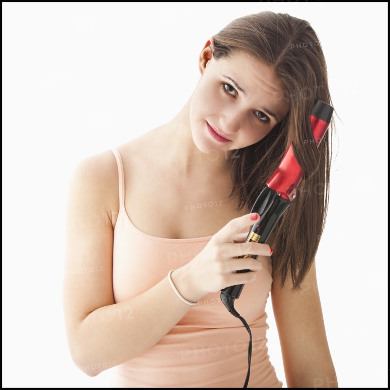 Studio portrait of young woman curling hair. Photo: Mike Kemp