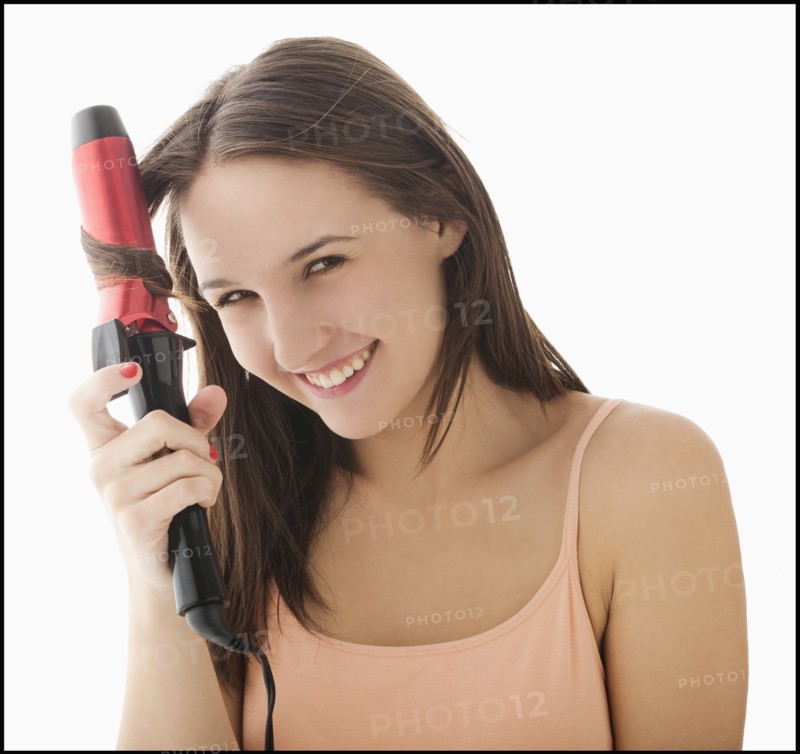 Studio portrait of young woman curling hair. Photo: Mike Kemp