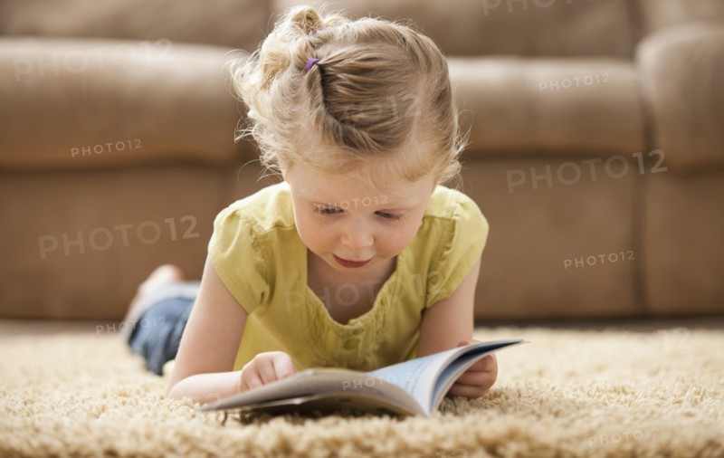 Girl (2-3) lying on rug, reading book. Photo : Mike Kemp