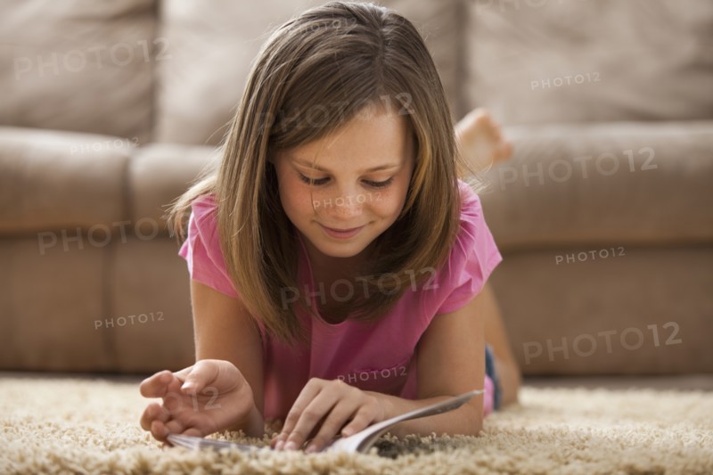 Girl (10-11) lying on rug, reading book. Photo : Mike Kemp