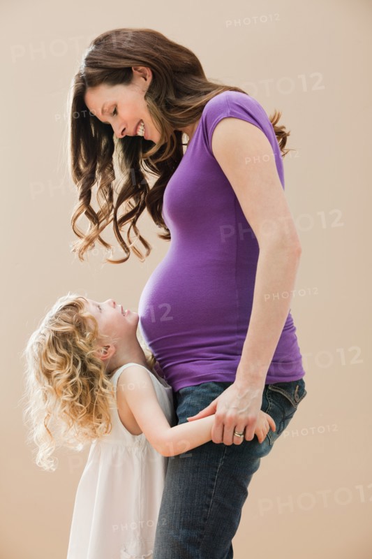 Portrait of girl (2-3) and pregnant mother holding hands. Photo: Mike Kemp