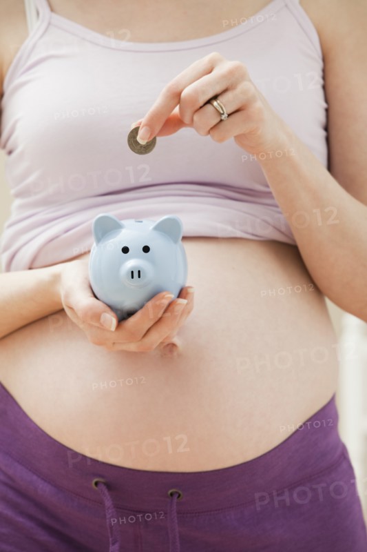 Young pregnant woman putting coin into blue piggybank. Photo : Mike Kemp