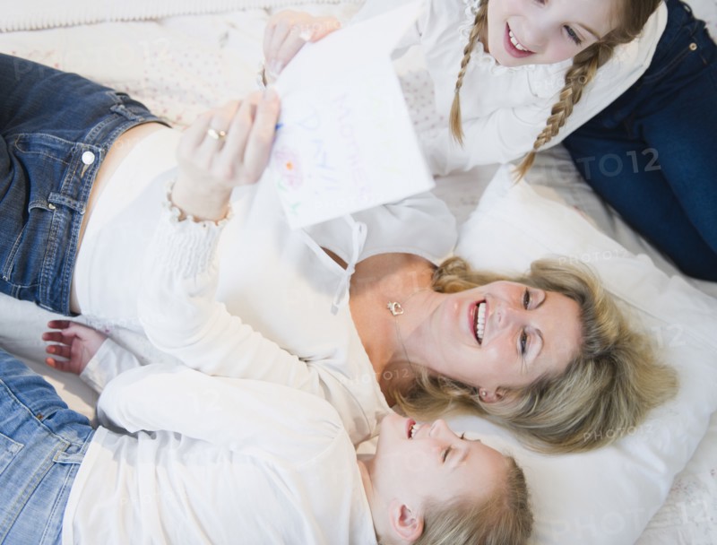 Mother and daughters (8-11) reading letter on bed. Photo : Jamie Grill Photography