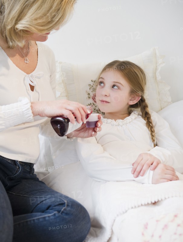 Mother giving medication to daughter (10-11) in bed. Photo : Jamie Grill Photography