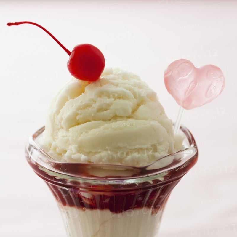 Close up of ice cream dessert with cherry on top and heart shaped decoration.