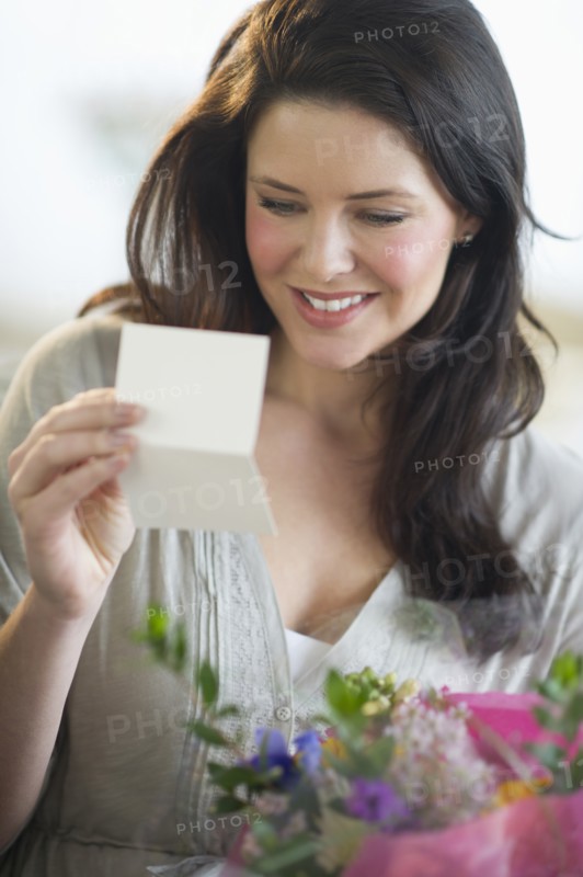 Young woman holding bouquet and reading greeting card.