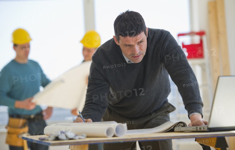 Architect preparing blueprintConstruction workers in background.