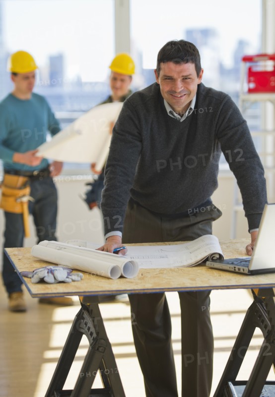 Architect preparing blueprintConstruction workers in background.