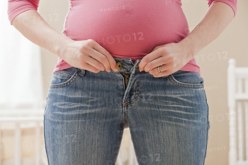 Young pregnant woman buttoning jeans. Photo : Mike Kemp