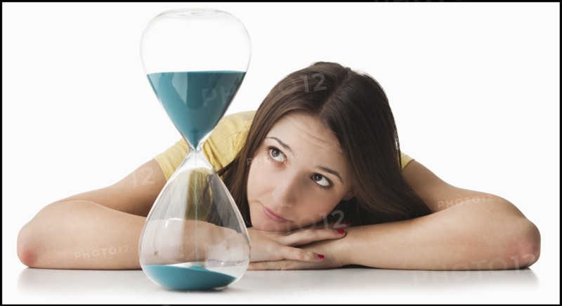 Young woman watching hourglass. Photo : Mike Kemp