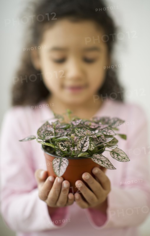 Portrait of defocused girl (6-7) holding potted plant.