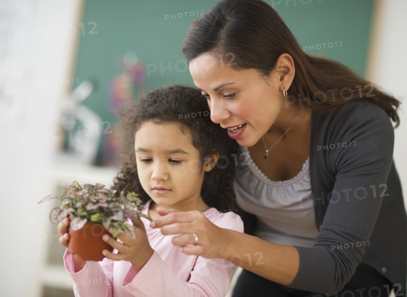 Girl (6-7) holding potted plant with female teacher.