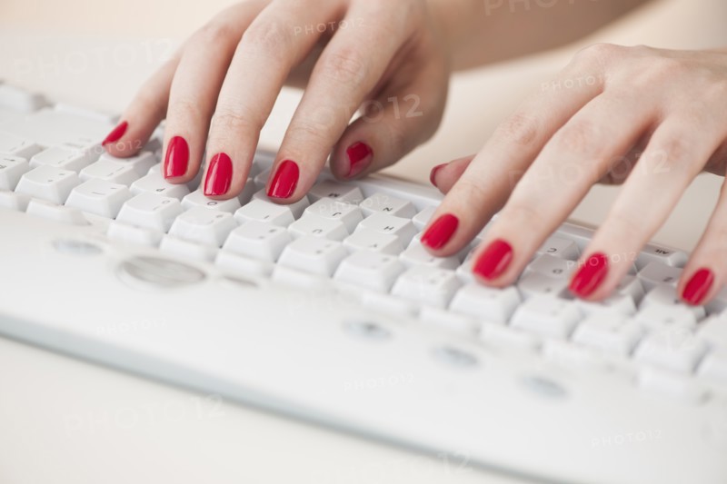 Close up of woman's fingers with red nail polish typing on computer keyboard.