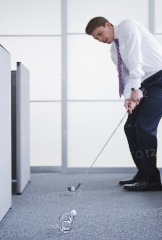 Businessman playing golf at office. Photo : Daniel Grill