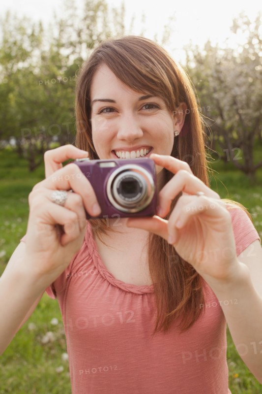 USA, Utah, Provo, Young woman holding digital camera in orchard. Photo : Mike Kemp