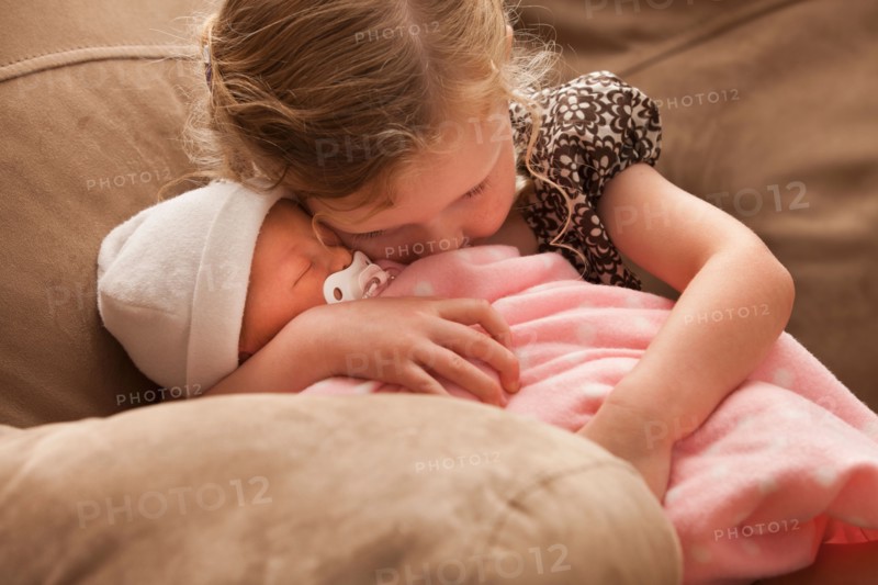 Girl (2-3) embracing baby sister on sofa. Photo : Mike Kemp