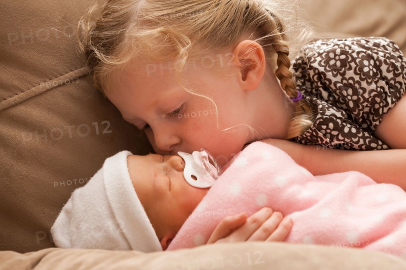 Girl (2-3) embracing baby sister on sofa. Photo : Mike Kemp