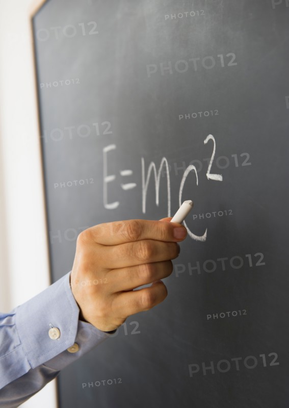Close-up of man's hand writing theory of relativity formula on blackboard.
