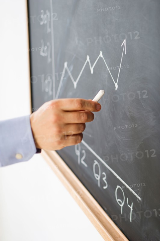 Close-up of man's hand drawing graph on blackboard.
