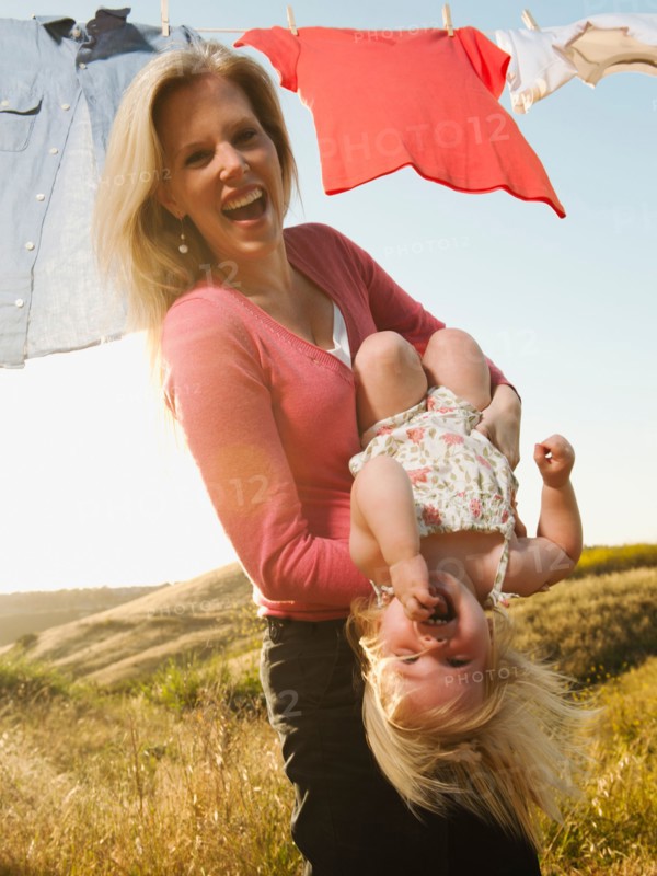 Mother playing with daughter (12-17 months) with laundry on clothesline in background.