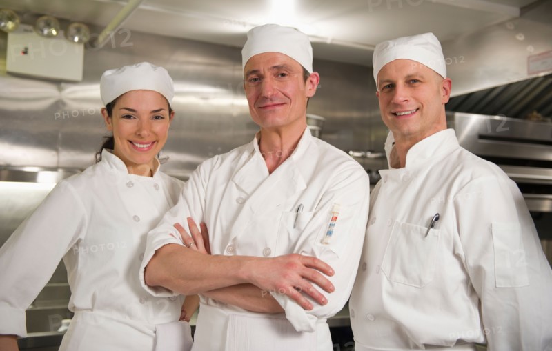 Three chefs posing in kitchen.