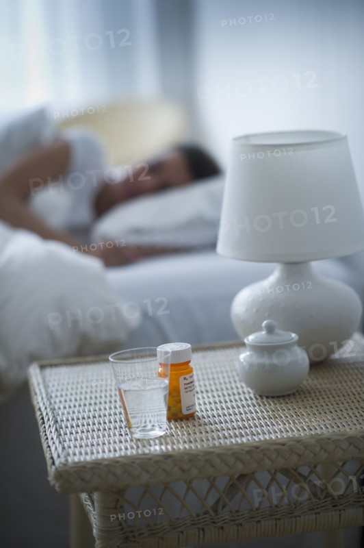 Sleeping pills bedside table with woman sleeping in background.