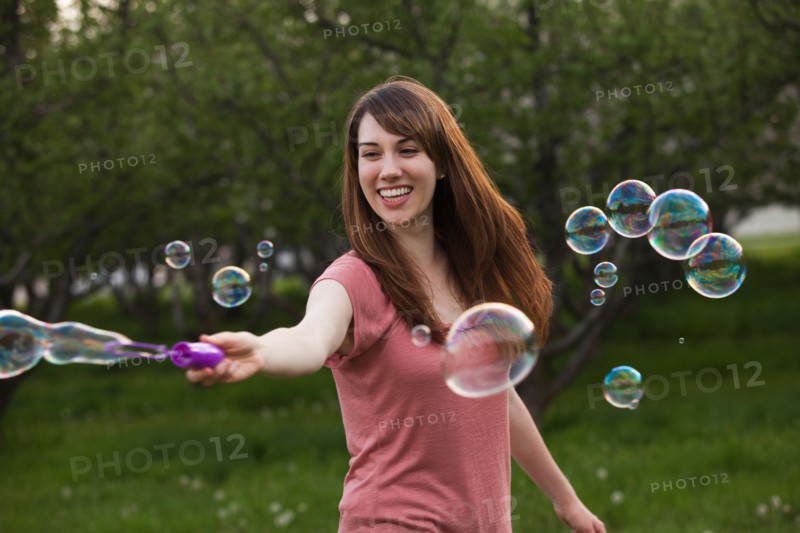 Young woman blowing bubbles in orchard. Photo : Mike Kemp