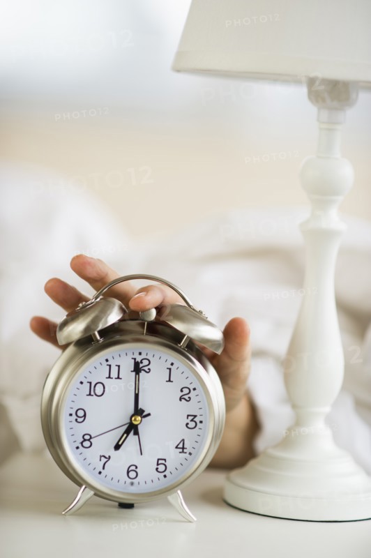 Close-up of man's hand reaching to alarm clock from bed.