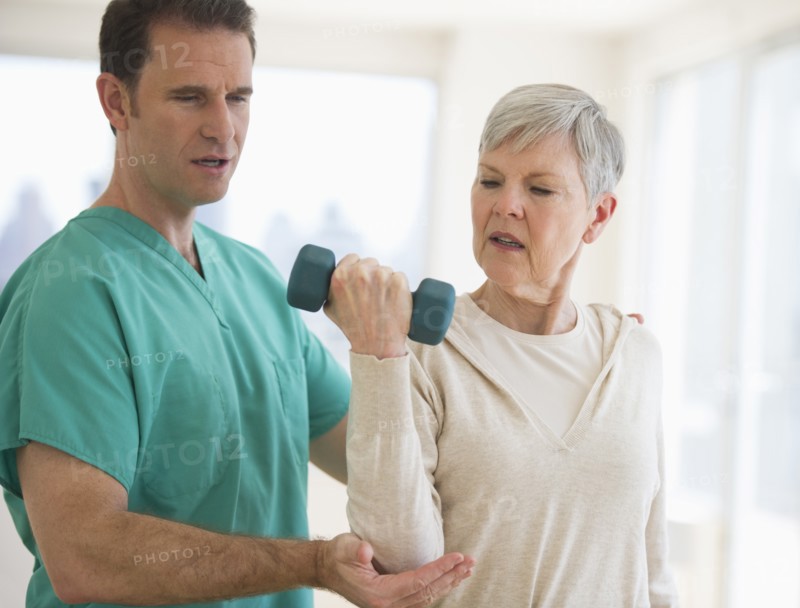 Man assisting  senior woman in weight lifting.