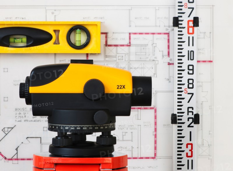 Close-up of theodolite, blueprint in the background.