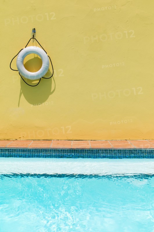 Lifebelt hanging on yellow wall by swimming pool.