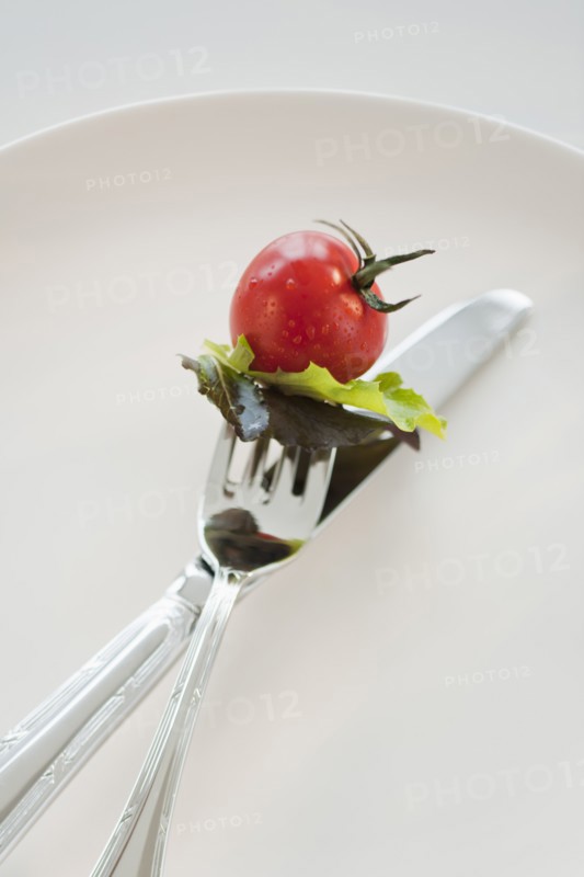 Cherry tomato and lettuce leaves on fork.