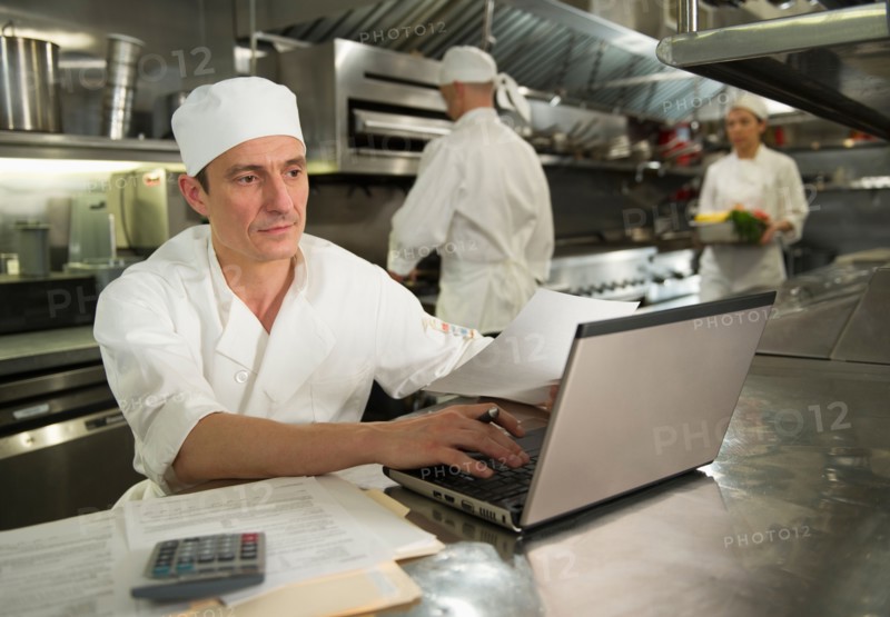 Chefs preparing food, one working on laptop.