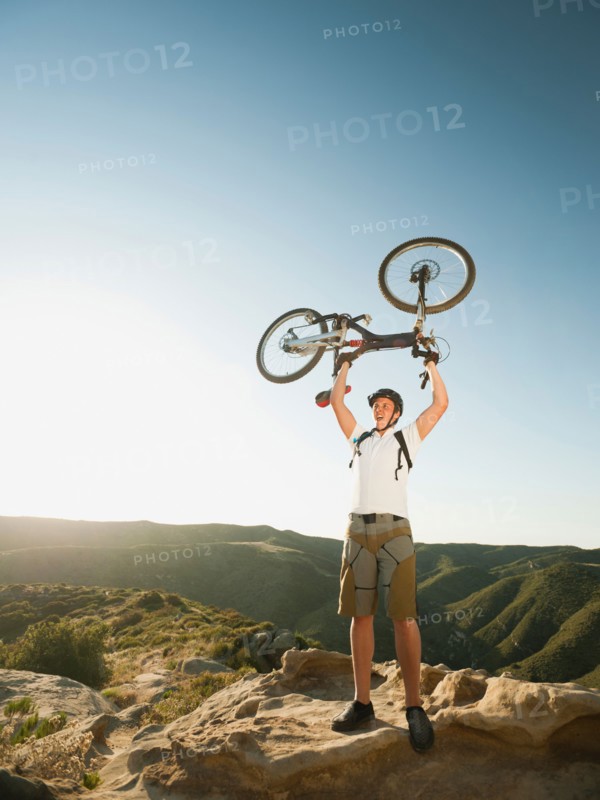 USA, California, Laguna Beach, Mountain biker on top of hill holding up his bike.